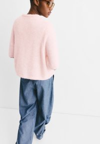 Pull en laine rose clair avec un col rond, associé à un pantalon rayé bleu ample. La tenue présente une coupe décontractée et une texture douce.