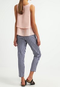 Jasnoróżowa bezrękawnikowa bluzka warstwowa z tyłu, w zestawie z granatowymi i białymi spodniami w paski o zwężanym kroju, noszona z czarnymi sandałami.