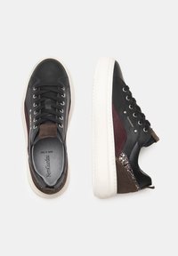 Sneaker in pelle nera con accenti borgogna e marroni. Presentano suole in gomma bianca, punta arrotondata e dettagli metallici decorativi.