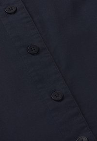 Gros plan sur un tissu noir avec une rangée de boutons noirs à quatre trous cousus sur une patte piquée.