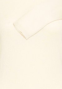 Manche de pull en tricot crème avec poignets côtelés, posée à plat sur un fond en tissu crème assorti.