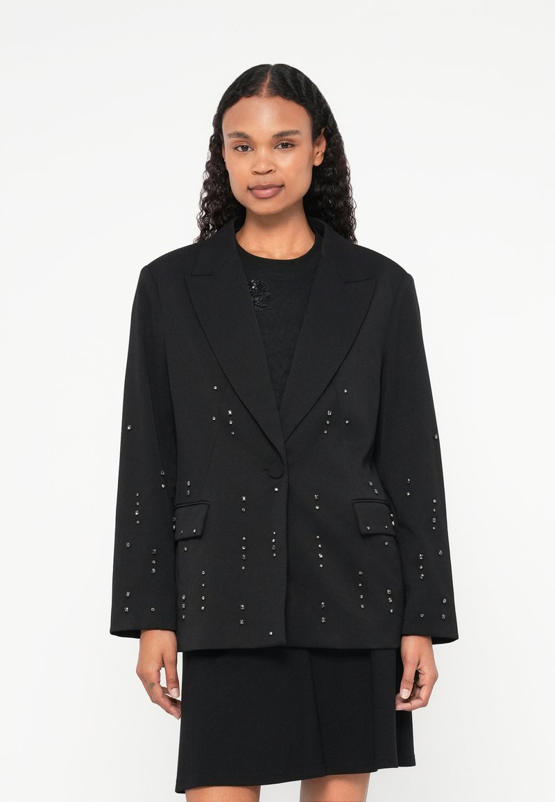 Blazer nero con borchie argento, chiusura a un bottone, risvolti a lancia e due tasche frontali. Forma strutturata con maniche lunghe.