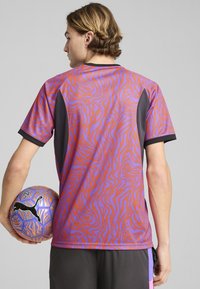 Camiseta atlética de manga corta en morado con un patrón de olas naranjas, con acentos de malla negra en los laterales y los hombros.