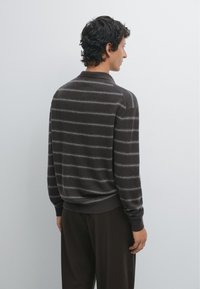 Maglione a righe marroni con una consistenza morbida, dotato di orlo e colletto a coste. Le righe sono grigie su uno sfondo scuro.