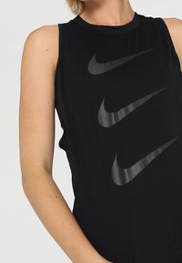 Czarna koszulka bez rękawów Nike z okrągłym dekoltem, z czterema błyszczącymi czarnymi logo swoosh w układzie przesuwnym. Miękki, lekki materiał.