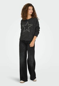 Pull en maille grise à manches longues avec un grand motif d'étoile entouré de clous argentés, associé à un jean noir à jambes larges.