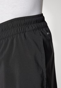 Zwarte sportshorts met een elastische tailleband, gladde textuur, zijzak en gestikte details. Bevat subtiele branding aan de zijkant.