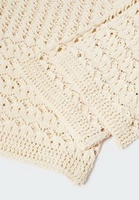Plaid di crema lavorata a maglia con pattern testurizzati e dettagli a trama aperta. Tessuto morbido e leggero che si adagia delicatamente, adatto per uso decorativo o funzionale.