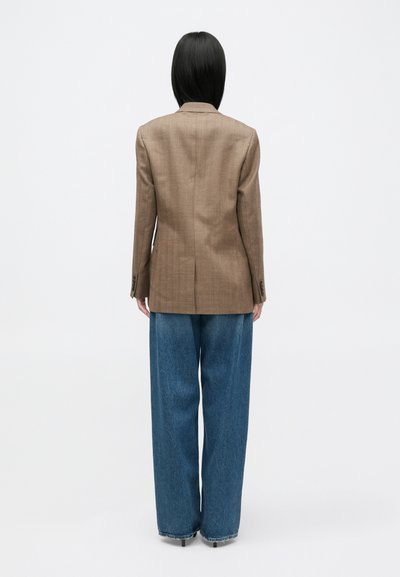 Blazer maro, texturat, cu un design ajustat, având o fenta unică, asortat cu blugi largi, decolorati, de culoare albastră deschisă.