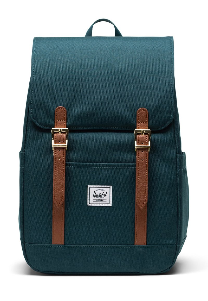 Sac à dos bleu foncé en tissu durable, avec des sangles en cuir marron, des boucles dorées et une poche avant avec une étiquette logo blanche.
