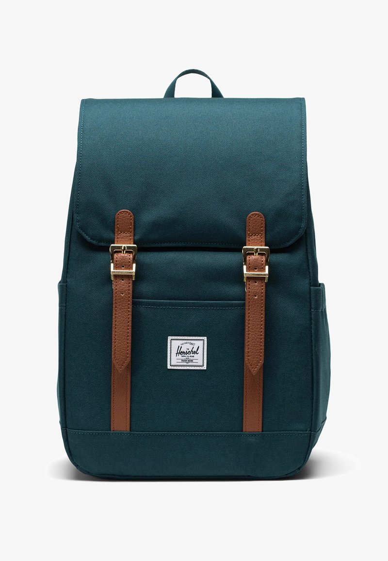 Mochila en verde oscuro hecha de un tejido duradero, con correas de cuero marrón, hebillas doradas y un bolsillo frontal con una etiqueta de logo blanca.