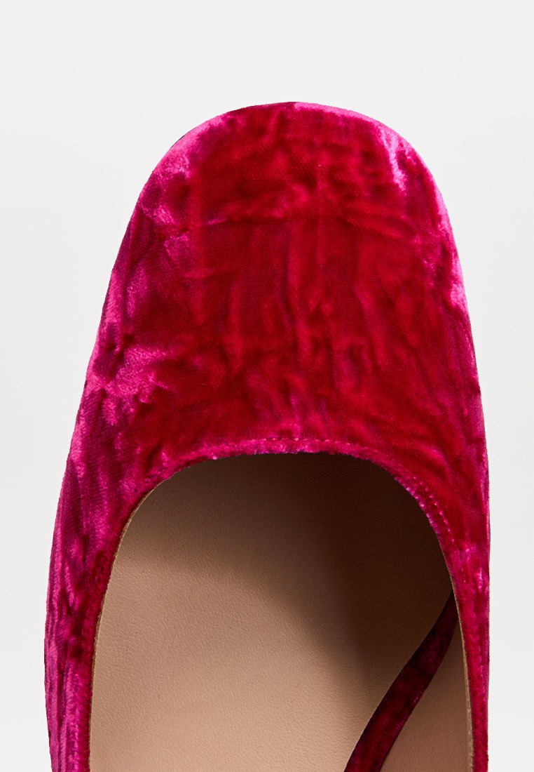 Scarpa di velluto rosa con punta arrotondata e texture liscia, caratterizzata da un design slip-on e una soletta di colore chiaro.