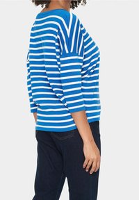 Lehký bavlněný top modrobílého proužkovaného vzoru s tříčtvrtečními rukávy, kulatým výstřihem a volnějším střihem. Kombinováno s tmavými džínami.
