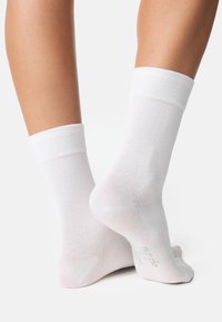 Calze a coste in cotone bianco, con cima a coste, texture liscia e talloni rinforzati. Dettaglio notevole include il nome del marchio stampato sulla suola.