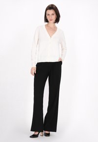 Cárdigan de marfil con cuello en V y botones en la parte delantera, combinado con pantalones de pierna ancha negros y tacones de punta negra. Texturas de tela suaves.