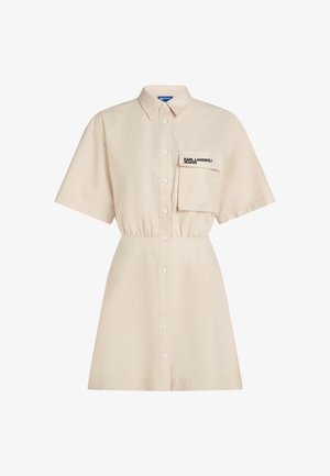 Béžové šaty košilového střihu s krátkými rukávy, zapínáním na knoflíky vpředu, klopovou náprsní kapsou označenou nápisem "KARL LAGERFELD JEANS" a staženým pasem.