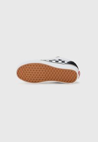 Lågprofil sneaker med svart och vit rutmönster, vita sidor och gummisulor med våffelmönster vända uppåt.