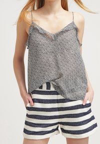 Mustavalkoinen kukkakuosiset toppi ohuilla olkaimilla, yhdistettynä kermanvärisiin ja tummansinisiksi raidoitettuihin shortseihin, joissa on teksturoitu kangas.