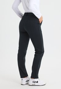 Donkerblauwe, strakke broek met een gladde textuur, voorzien van achterzakken en een middelhoge tailleband, gecombineerd met witte Nike hardloopschoenen.