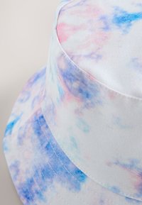 Chapeau bob en tissu blanc avec un motif tie-dye dans des tons pastel rose, bleu et violet, doté d'un large bord et de coutures visibles.