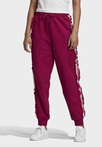 Bordové tepláky s volánkovými akcenty po stranách, mají stahovací pas a zúžené nohavice. Spárovány s bílými teniskami.