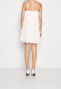 Vit lagerklänning i lätt tyg, med tunna axelband och ett lagerdesign. Bärs med vita högklackade skor.