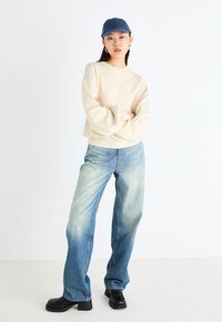 Cream sweater, light blue jeans, black platform boots, and a blue cap. The jeans have a faded look with a loose fit and slight distressing.