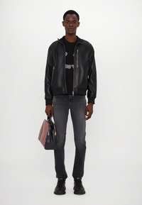 Μαύρο δερμάτινο μπόμμερ με ριμπ μανσέτες, μαύρη μπλουζα γραφικών, γκρι τζιν και μια πολυχρωμη ριγέ τσάντα. Μαύρα παπούτσια.