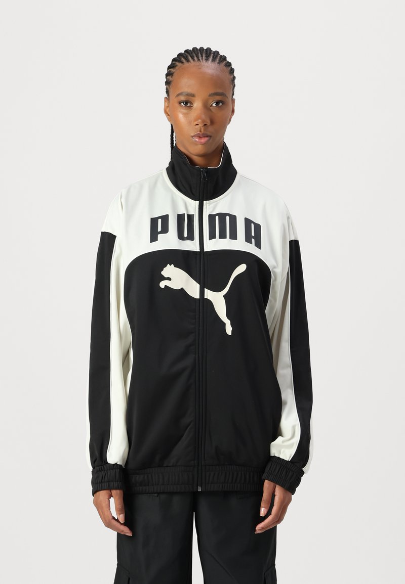 PUMA sportlik jakk, millel on must keha ja valged aktsendid, kõrge krae, täiskraan ja suur logo rinna peal. Elastsed mansetid.