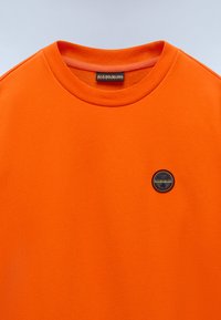 T-shirt in cotone arancione con collo tondo, scollatura a costine e un’etichetta logo circolare sul petto per un Brand distintivo.