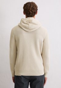 Hellbeige Kapuzenpullover mit strukturiertem Strickmuster, langen Ärmeln und tailliertem Saum. Sichtbare Nähte an den Schultern.