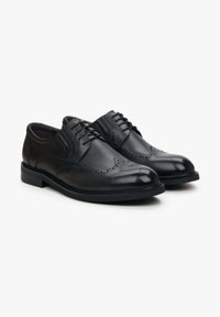 Czarne skórzane buty, z polerowanym wykończeniem, z detalami w stylu brogue i sznurówkami. Posiadają okrągły czubek i płaską gumową podeszwę.