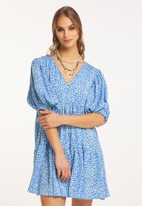 Rochie florală albastră cu decolteu în V, mâneci bufante și fustă în straturi. Fabricată dintr-un material ușor, cu o textură moale și un model jucăuș.
