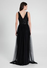 Schwarzes Abendkleid mit tiefem V-Ausschnitt, verziertem Pailletten-Oberteil und fließendem, durchscheinendem Überwurf von der Taille bis zum Boden.