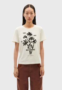 White cotton t-shirt featuring a black floral graphic print and the text "THE ART OF BECOMING" in a contemporary font. Short sleeves.