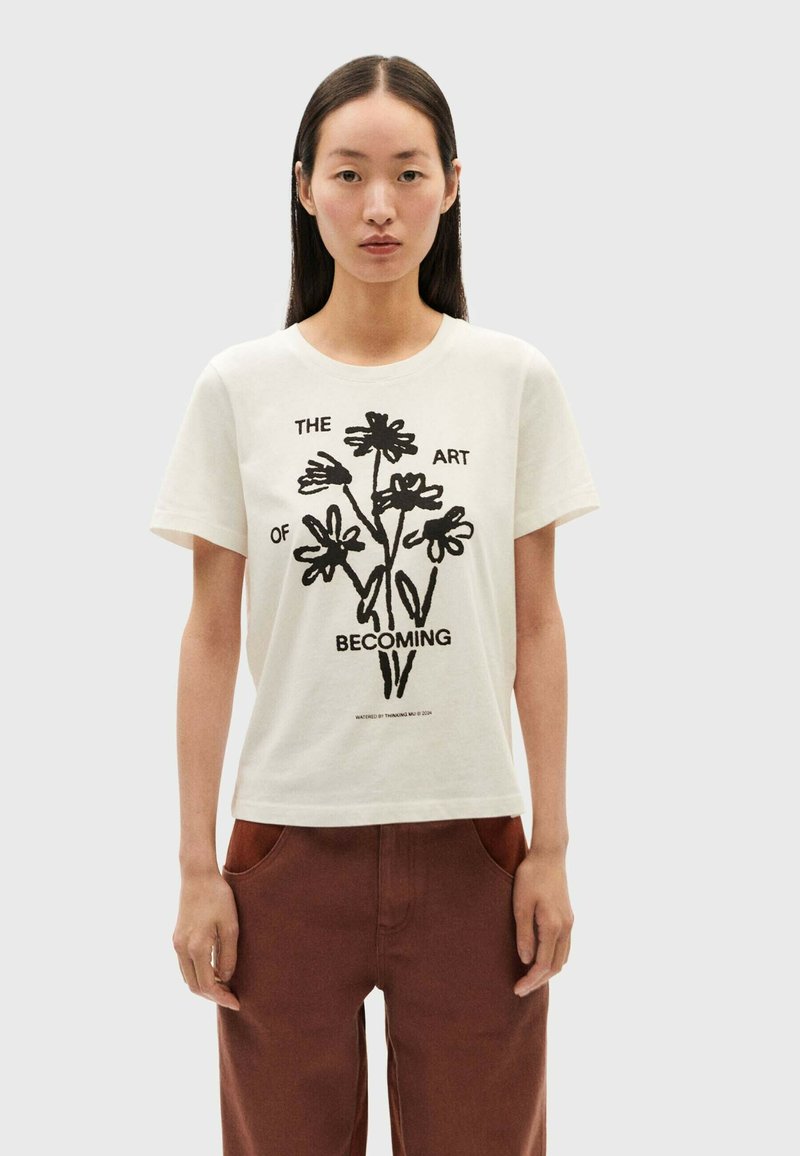 White cotton t-shirt featuring a black floral graphic print and the text "THE ART OF BECOMING" in a contemporary font. Short sleeves.