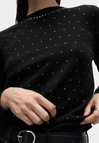 Pull noir avec une finition texturée, décoré de strass dispersés sur le tissu et d'un détail de col orné de strass.