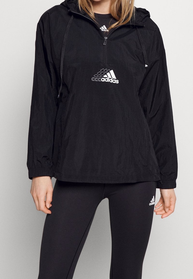 Zwarte windbreaker gemaakt van lichtgewicht stof met een capuchon, uitgerust met een halve rits aan de voorkant en een wit Adidas-logo op de borst.