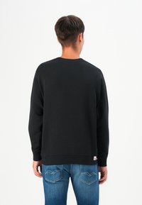 Black sweatshirt with a crew neck and long sleeves, featuring ribbed cuffs and hem, paired with blue denim jeans.
