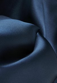 Mörkblå satintyg med en slät, glansig yta, som har mjuka veck och subtil reflektion av ljus, vilket förstärker dess rika färgdjup.