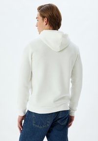 Capuchon sweatshirt in off-white katoenmix met ribbels aan de mouwen en onderkant. Kenmerkend is de gladde textuur en het minimalistische ontwerp.