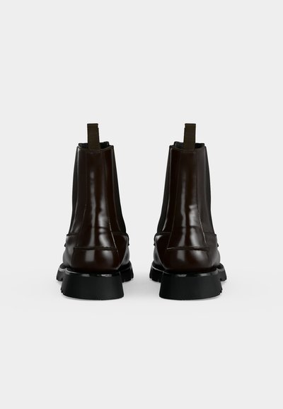 Paire de bottines en cuir marron foncé avec des semelles épaisses noires, vues de dos sur un fond clair uni.