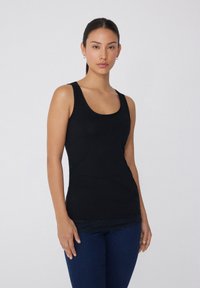 Top sin mangas negro hecho de una tela suave con escote en forma de barco y un borde de encaje en el dobladillo, combinado con pantalones de mezclilla azules.