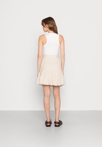 Top branco sem mangas combinado com uma saia mini evasê em padrão xadrez nas cores bege e creme, com dois bolsos laterais e um tecido texturizado.