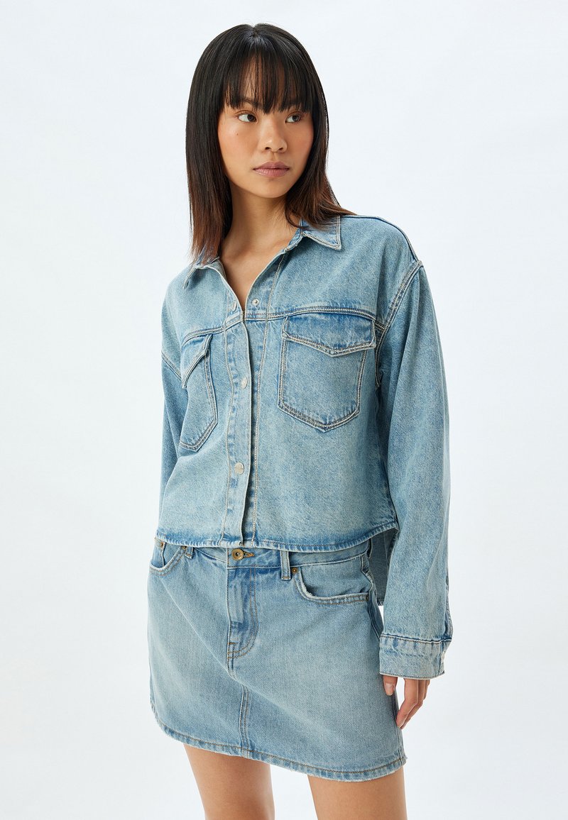 Ljusblå denimjacka med två bröstfickor, knappstängning och matchande denimkjol. Rakt snitt med en lätt fransad nederkant.