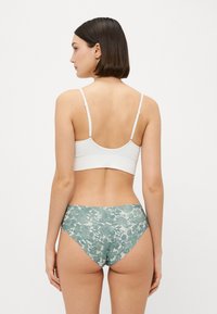 Fehér, cropped fazonú bralette vékony pántokkal, zöld mintás, magas derekú bugyival párosítva, amely puha, textúrált anyagból készült.