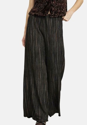 Pantalones negros de pierna ancha con rayas metálicas verticales, combinados con un top oscuro de lentejuelas y zapatos negros de punta abierta.