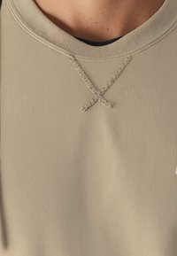 Felpa beige a coste con scollatura rotonda, caratterizzata da dettagli di cucitura visibili e una texture sottile. Non sono presenti elementi grafici.