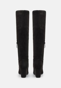 Botas altas hasta la rodilla de ante negro con tacón cuadrado, que cuentan con una cremallera en el lateral, textura suave y detalles de costura.