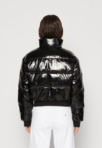 Giacca a piumino nera con una texture lucida e trapuntata, collo alto e polsini a costine; design corto con silhouette aderente.